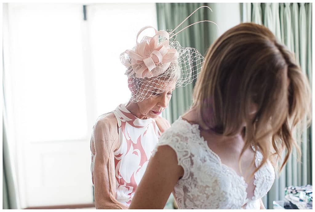 Mother of the bride doing up bride's dress Barnsley House Photographer